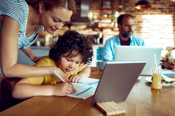 Mother helping son with homework as father works on laptop in kitchen