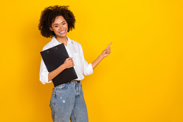 Portrait of attractive lady hold clipboard indicate finger empty space isolated on yellow color...