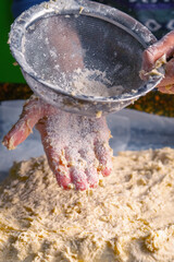 Close up female experienced chef dusting the dough to pizza with flour.