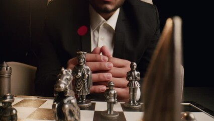 A young respectable indian man in a business suit plays a chess, crosses fingers, thinks and makes a move. Metal figures stand on a chessboard. The concept of intellectual aristocratic leisure. Close