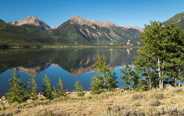 Naklejka premium Reflections on the west Twin Lake are 13,939 Foot Mount Hope, 13,290 & 13,333 Foot Twin Peaks, with 13,783 Foot Rinker Peak in the early Summer morning of August in central Colorado.
