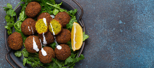 Plate of fried falafel balls served with fresh green cilantro and lemon top view on rustic concrete background. Traditional vegan dish of Middle Eastern cuisine, space for text - 769945209