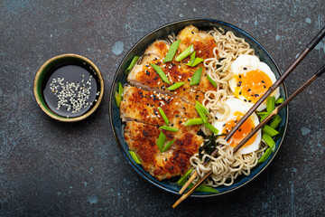 Asian noodles ramen soup with deep fried panko chicken fillet and boiled eggs in ceramic bowl with chop sticks and soy sauce on stone rustic background top view - 769950881