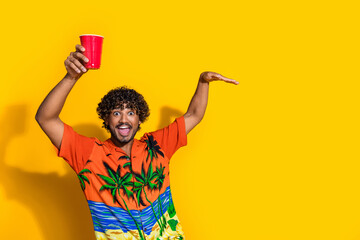 Photo of optimistic man with afro hairdo dressed print shirt raising up plastic cup dancing at...