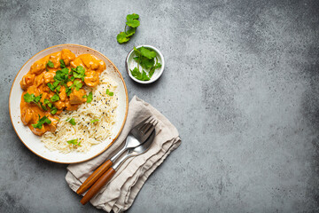 Traditional Indian dish chicken curry with basmati rice and fresh cilantro on rustic white plate on gray concrete table background from above. Indian dinner meal