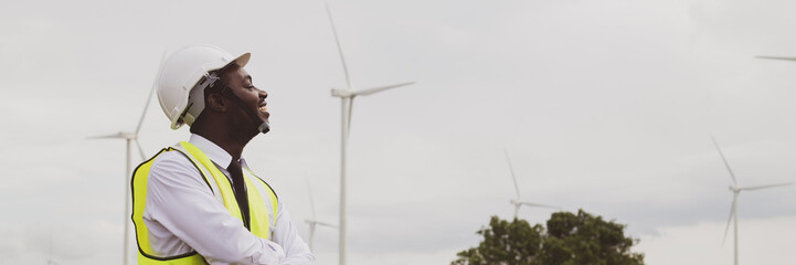 African engineer stand with smile near the wind turbine for inspect the operation of large wind turbines that converts wind energy into electrical energy