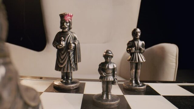 The antique and vintage metal chess figures stand on a chessboard. The concept of intellectual aristocratic leisure. Close up. Selective focus. Slow motion mode.