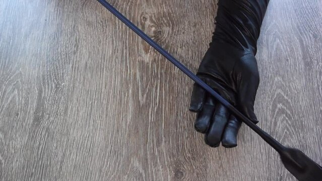 Horizontal Full HD video. Top view. Woman holds riding hunting crop, stack, short thin cane with leather loop at end, whip for horse riding, adult love games. Female hand in black gloves close up. Toy