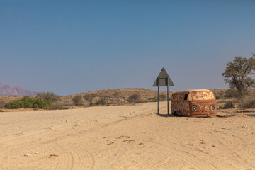 The rusting hulk of a vehicle stands abandoned along a desert road in central Namibia in mute...