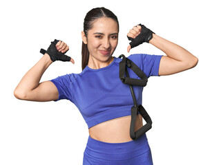 Athletic young Caucasian woman with resistance band on studio background feels proud and self...