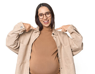 Pregnant young Caucasian woman showcasing maternity on studio background surprised pointing with...