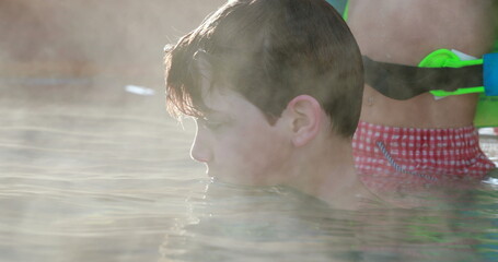 Child inside warm swimming pool water, heated water evaporating