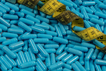 Blue weight loss pills and measuring tape symbolizing slimming