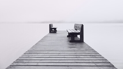 Two benches opposite each other on the pier and fog on the lake.