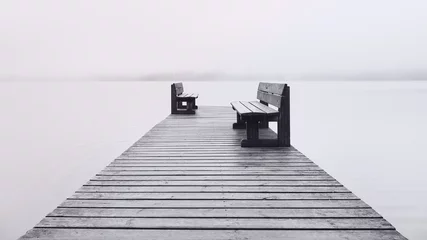 Fotobehang Pier Two benches opposite each other on the pier and fog on the lake.  © ROMAN BELIAKOV