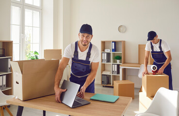 Young mover man packing laptop for moving, individual or company worker job moving office things, possessions, boxes, busy workmen professional team wearing uniform helping to change residence 