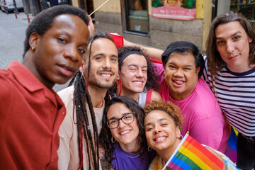 A group of people pose for a selfie, one of them holding a rainbow flag.
one of them holding a...