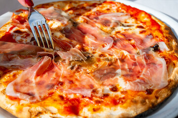 Eating of fresh baked pizza dish in italian pizzeria restaurant, Prosciutto di Parma