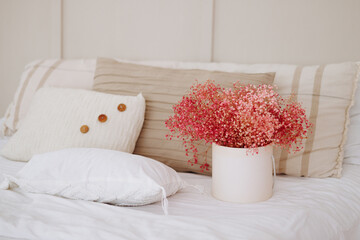 Serene bedroom with a neatly made bed, adorned with textured pillows and a vibrant bouquet of pink...