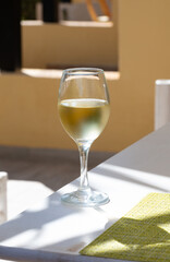 Glass of cold white wine on white terrace table outdoor in sunny day