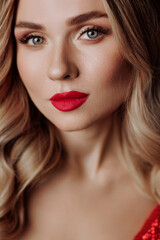 Fototapeta na wymiar Beautiful blonde woman model in a red dress on a black background in a red shiny dress with makeup and bright red lips. Concept fashion industry, makeup artists or advertising of fragrance, cosmetics.