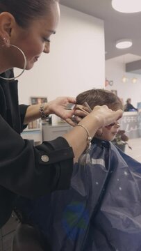 Woman hairdresser cutting a child's hair with comb and scissors in a salon