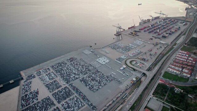 Overhead view capturing the sprawling infrastructure of an industrial maritime port filled with cargo, containers, and vehicles at dusk.