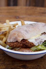 Closeup view of a fried chicken steak sandwich with cheese, lettuce and mayonnaise on the wooden table. 