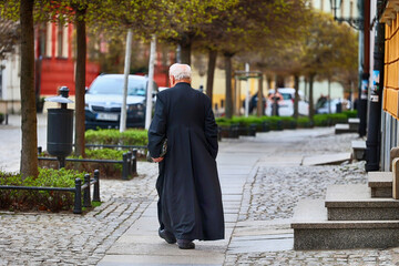 Ksiądz katolicki z teczką idzie ulicą.  - obrazy, fototapety, plakaty