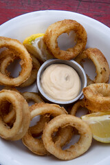 Seafood. Top view of delicious fried squid rings with lemon and a dipping sauce in a white bowl.	
