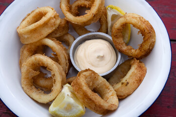 Seafood. Top view of delicious fried squid rings with lemon and a dipping sauce in a white bowl.	
