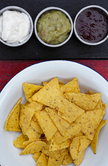 Mexican food. Top view of nachos in a white bowl and three dipping sauces of cheddar cheese, sweet chili and guacamole.