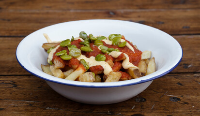 Fried food. Closeup view of french fries with a spicy sauce and beans, in a white bowl on the table.	