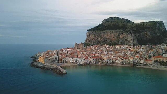 Aerial view of Cefalu, Sicily. Establishing cinematic drone shot of famous travel destination of Italy, view of Cefalu Cathedral. Slow drone shot travelling toward the historic town from the sea.