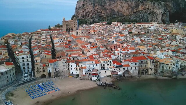 Aerial view of Cefalu, Sicily. Cinematic drone shot of famous travel destination of Italy, view of Cefalu Cathedral and beach. Slow drone shot travelling in a wide orbit above the historic town.