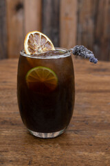 Night cocktails. Closeup view of an alcoholic drink with fernet, cynar, sliced lime and lavender with a rustic wooden background