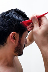 Hombre joven aplicando tinte natural en el pelo con brocha roja para cubrir sus canas. Tintura a...