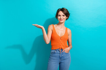 Portrait of gorgeous girl with short hairdo wear orange knit top palm demonstrate offer empty space isolated on blue color background