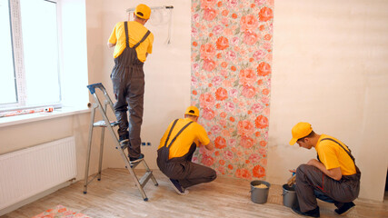 Brigade of builders hang wallpaper in the apartment. Masters make repairs.