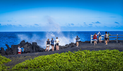View of Black Sand Park in Maui, Hawaii, with people watching large waves breaking against shore and blue sky in background