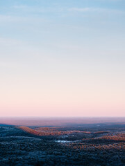 A winter scene as viewed from on top of a mountain in New England. The forest is covered in ice and snow. The sun is setting creating shadows on the landscape and orange, blue, and pink colors.