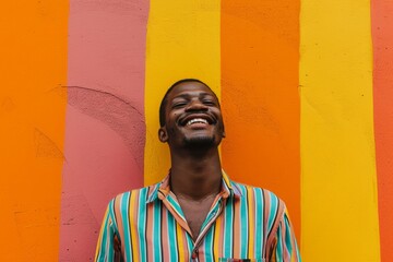 Joyful man smiling with eyes closed against a vibrant striped orange and yellow wall.