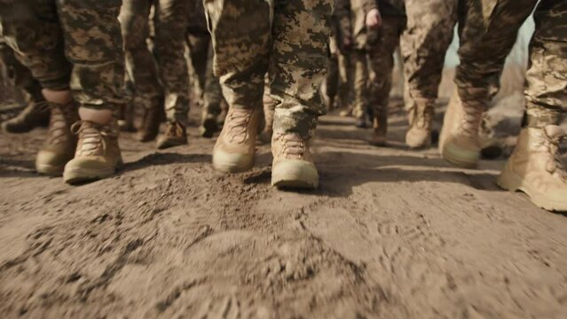 A close-up reveals the dusty boots of soldiers marching in unison through sandy terrain, symbolizing the unity and determination of the military march. 