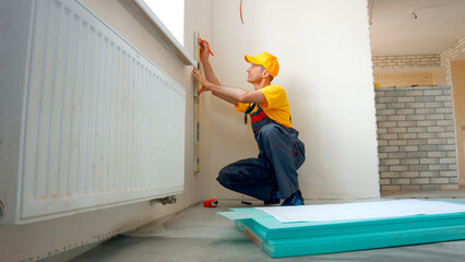 Builder makes markings on the wall. Worker making apartment renovation by project.