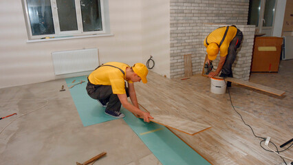 Workers lay laminate flooring in a new home. Internal repair works.