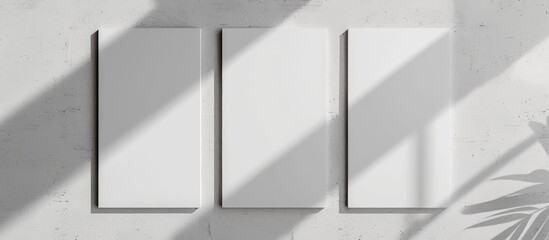 Three blank white vertical rectangular poster mockups with gentle shadows on a neutral light grey concrete wall backdrop. Overhead view, flat lay.