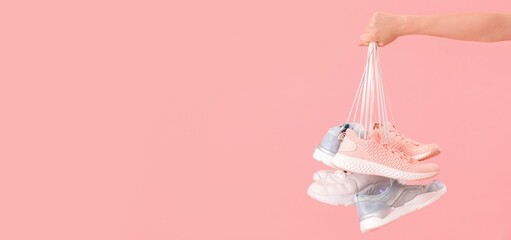 Female hand with many sneakers on pink background with space for text