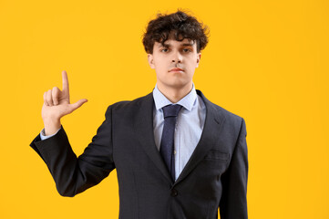 Young businessman showing loser gesture on yellow background