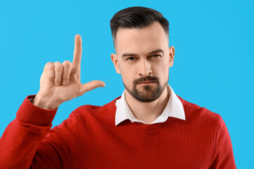 Handsome man showing loser gesture on blue background, closeup