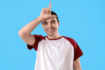 Young man showing loser gesture on blue background